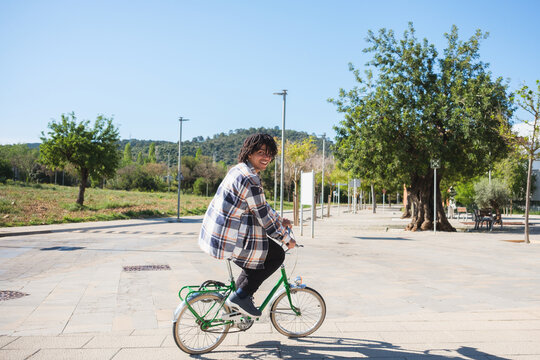 A happy young man is riding a green bicycle along a park path