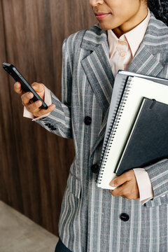 Businesswoman Checking Smartphone While Holding Notebooks