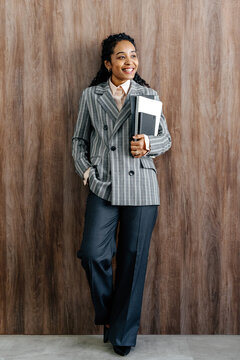 Businesswoman Holding Notebooks While Standing Against Wooden Wall