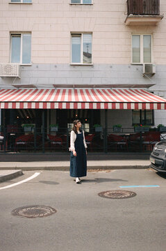 Young woman stands on street near cafe with red and white awning