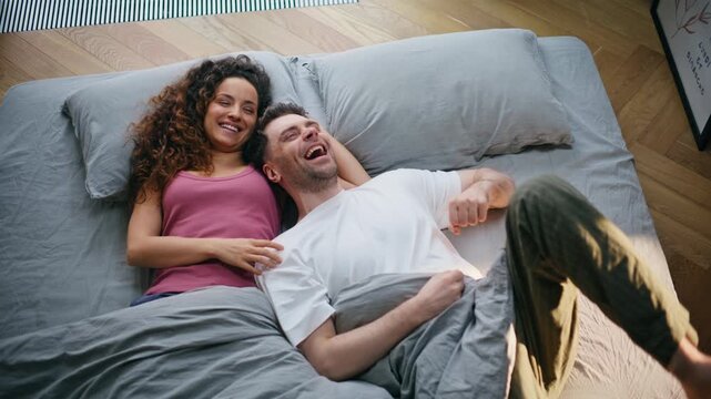 Couple laughing together bed morning. Playful young pair joking home bedroom.