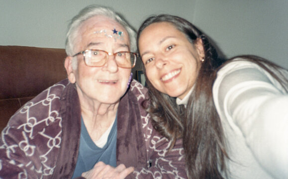 Woman takes a selfie while caring for her father at home.