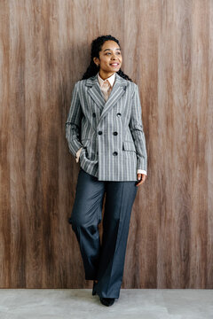 Professional Woman in Plaid Blazer Standing Against Wooden Wall