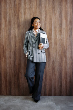Businesswoman Holding Notebooks While Standing Against Wooden Wall