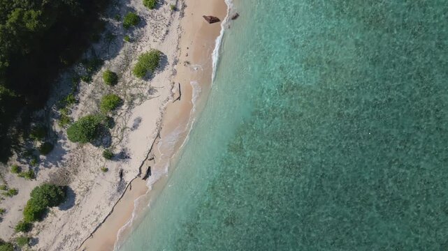 Top down aerial view of quiet beach and tropical waters with small gentle waves in slow motion at Tabuhan Island, East Java