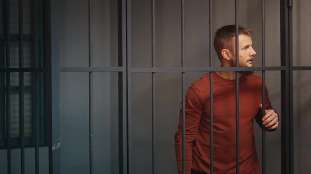 Nervous young arrested man pacing behind jail cell bars, waiting for release