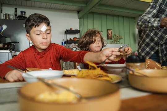 Siblings enjoying breakfast pancakes together at home kitchen