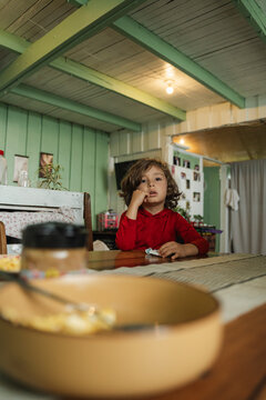 Little one contemplating at wooden table indoors