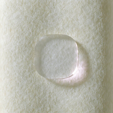 Clear droplet resting on textured cotton paper soft lighting and subtle shadow water drop liquid