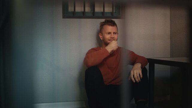 Stressed arrested man sitting on a jail cell floor, feeling shame and guilt