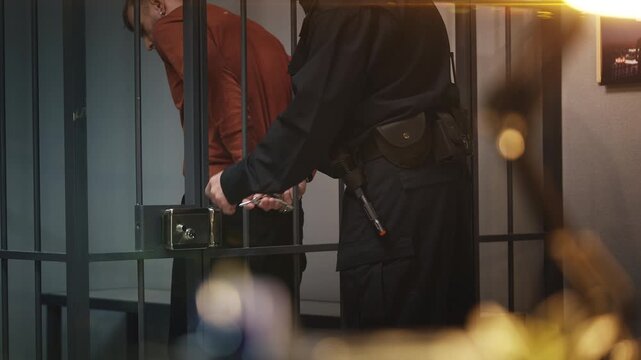 Police officer removing handcuffs and escorting a detainee out of jail cell