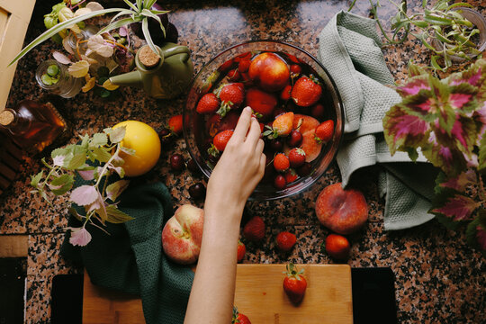 Hand reaching for strawberries in a bowl on a kitchen counter