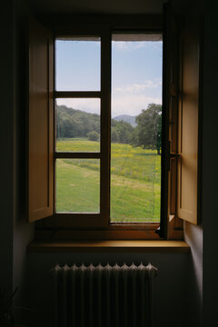 Open window view of green field and mountains in daylight