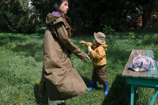 Mother and child walking hand in hand in a park wearing raincoats