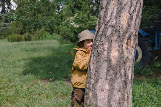 Child hiding behind a tree while mother sits in a garden