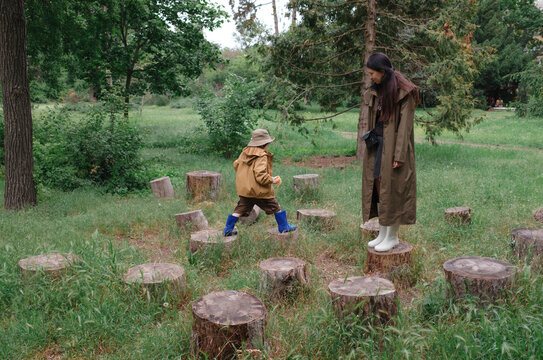 Mother and son jumping on tree stumps in a botanical garden