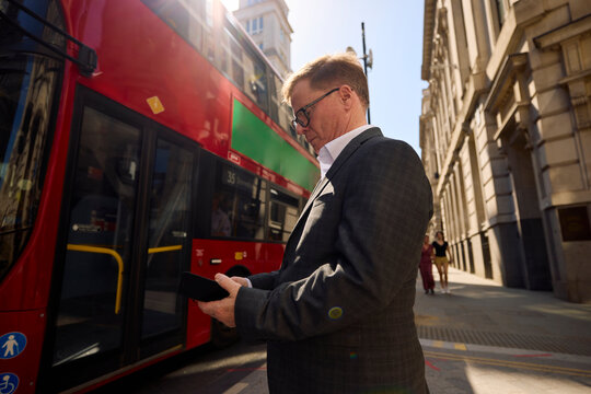 Businessman stands on the street in London, checking his phone