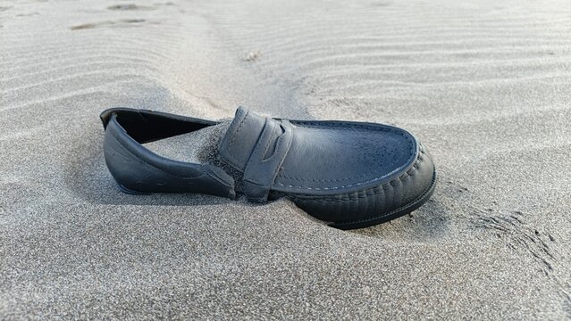 Black Leather Loafer Partially Buried in Volcanic Sand Creating a Solitary Coastal Story at a Beach in Yogyakarta Indonesia