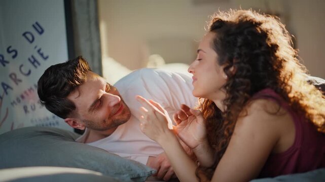 Loving couple relaxing bed morning sunlight. Happy man woman laughing bedroom.