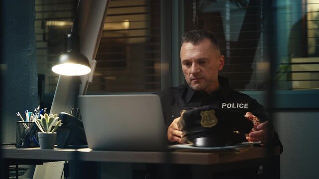Calm police officer eating a donut and drinking coffee during a night shift