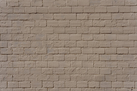 Rectangular bricks are covered with peeling beige paint. Cracked layers and rough textures create an aged brickwork background.