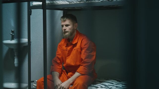 Depressed young male inmate sitting on a prison bed, feeling remorse