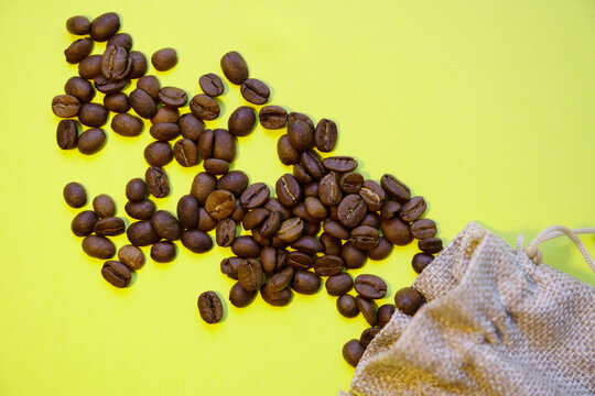 Roasted beans spilling from a sack on a yellow background