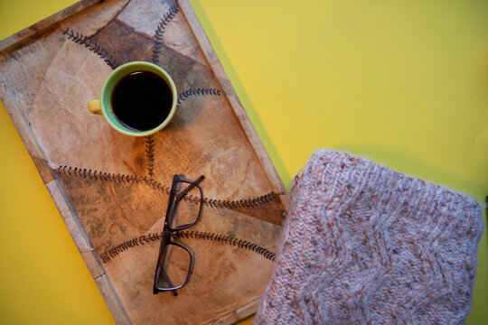 A cup of coffee on a tray with some glasses and a knitted garment.