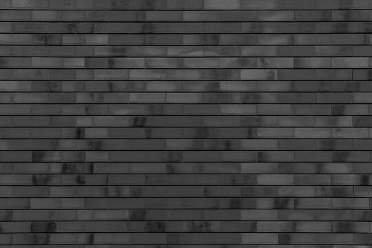 Black clinker brick wall with smooth rectangular bricks and dark thin seams. Variegated dark surface with subtle monochrome gradients for a contemporary monochrome architectural background.