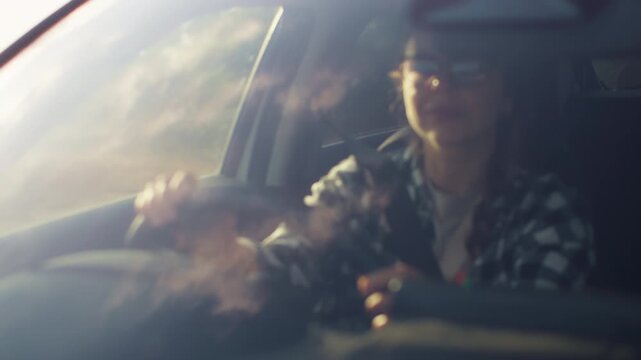A Caucasian woman behind the wheel of a car. A young woman is driving whether on a trip or to work along the road in the sunlight.