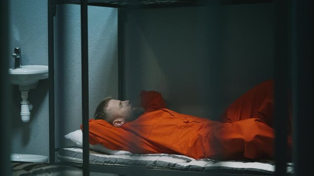 Male prisoner in an orange prison uniform lying on a bed, serving a sentence