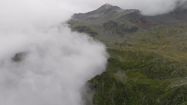 Aerial drone view of Tyrol mountain landscape with rugged Alpine peaks rising through clouds surrounded by green fields spectacular nature scenery and European tourism