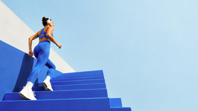 Athletic woman running up stairs against a clear sky.