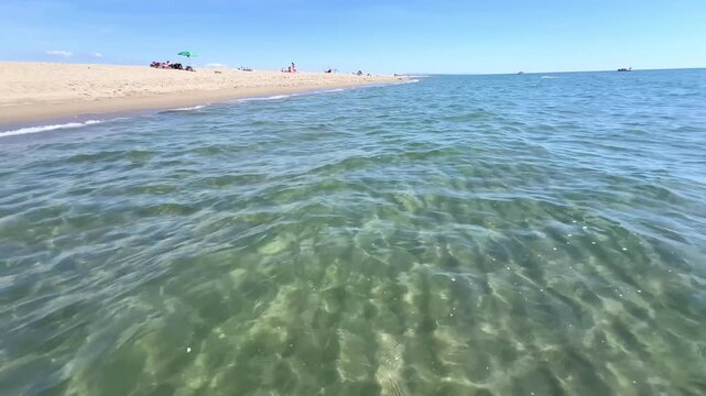 Sea water ripples texture clear turquoise surface at sand beach in Tuscany, Italy