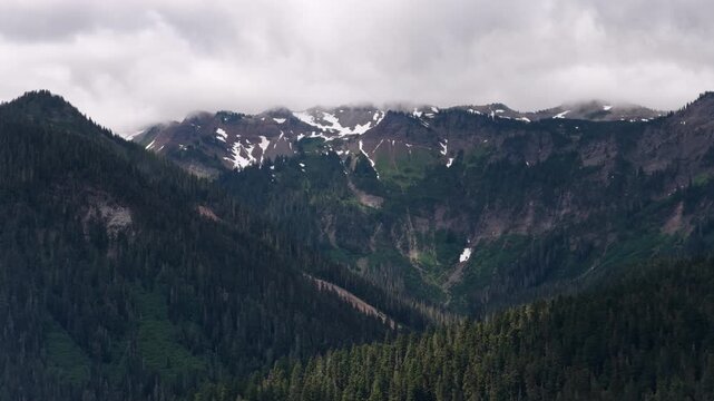 Wide aerial of Cascade Mountains and valleys in Gifford Pinchot National Forest with deep canyons and patches of snow in summer near Packwod Washington