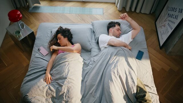 Couple waking up bed checking phones morning. Young people startled reaction