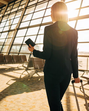 A professional blonde businesswoman walking through a bright modern airport terminal with her suitcase ready for a business trip abroad