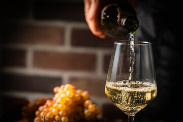 Obraz premium Pouring white wine into the glass on rustic dark background. Pour alcohol, winery concept.
