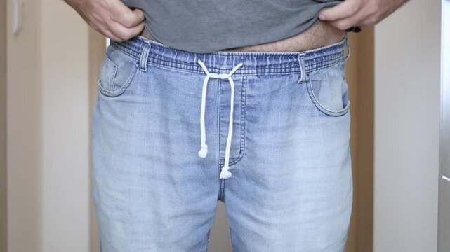 Overweight Man Trying to Put On Tight Jeans Closeup. Man with Big Belly Trying to Button Tight Jeans