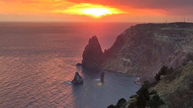 Golden sunset illuminates jagged coastal cliffs overlooking the deep blue sea at twilight. Static wide shot.