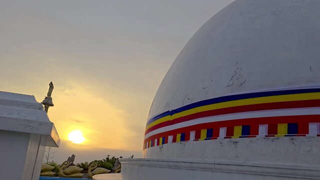 Panoramic sunrise view of a Buddhist stupa on a mountain peak with a Buddhist flag below, illuminated by the first sunlight against a dramatic sky. 4K