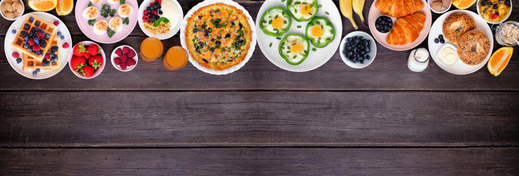 Breakfast or brunch top border on a dark wood banner background. Overhead view. Assorted fruits and sweet and savory food items. Copy space.