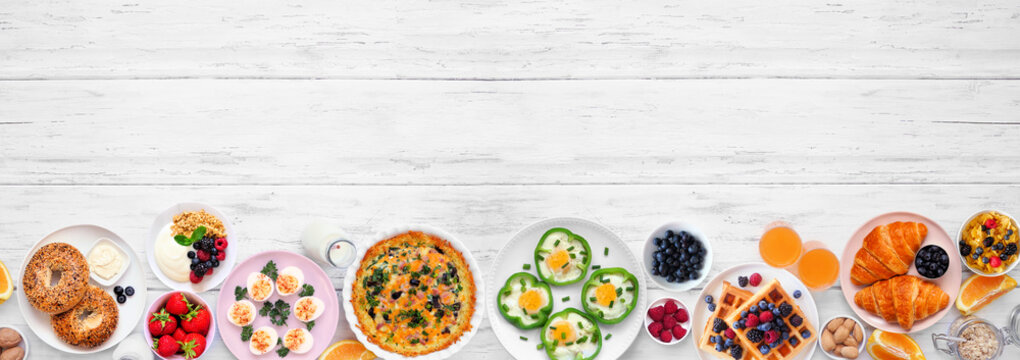 Breakfast or brunch bottom border on a white wood banner background. Top view. Assortment of fruits and sweet and savory food items. Copy space.