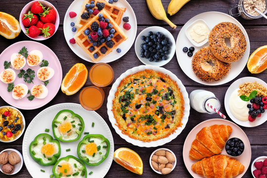 Breakfast or brunch table scene on a dark wood background. Top view. Assortment of fruits and sweet and savory food items.