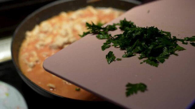 Adding fresh chopped parsley to simmering chicken meat in tomato sauce close up.