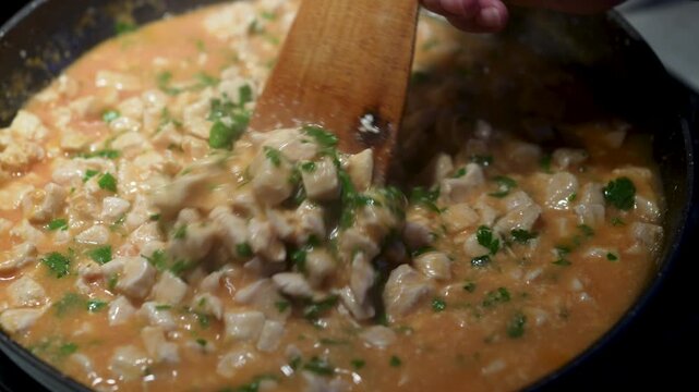Stirring simmering chicken goulash with wooden spatula in frying pan close up
