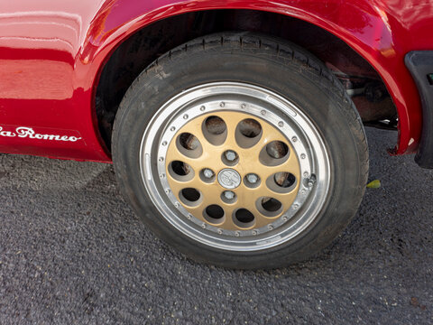 TAVERNES BLANQUES, SPAIN - JUNE 14, 2026.Close up of vintage gold and silver alloy wheel rim with Alfa Romeo logo on classic red car