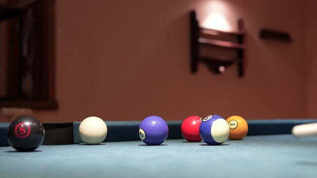 Close up shot of a striped number fifteen pool ball rolling into a middle side pocket on a blue felt billiard table, followed by the white cue ball falling into the same pocket right after.