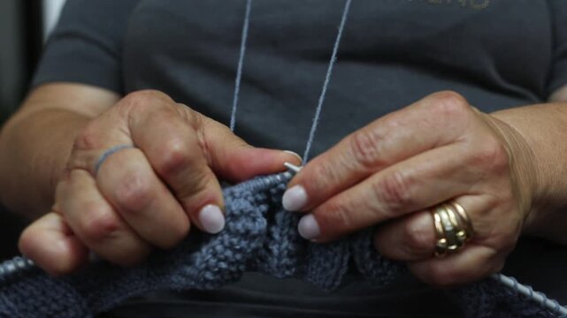 Close-up view of a woman's hands skillfully knitting with needles and gray yarn, showing the process of creating a warm handmade sweater, a traditional craft and relaxing pastime for winter