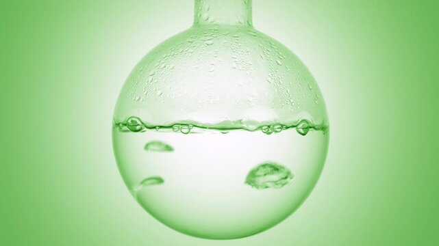 Close-up shot of bubbles creating motion as they rise through crystal clear liquid boiling in a round-bottom flask condensing on it's walls on green ramp background